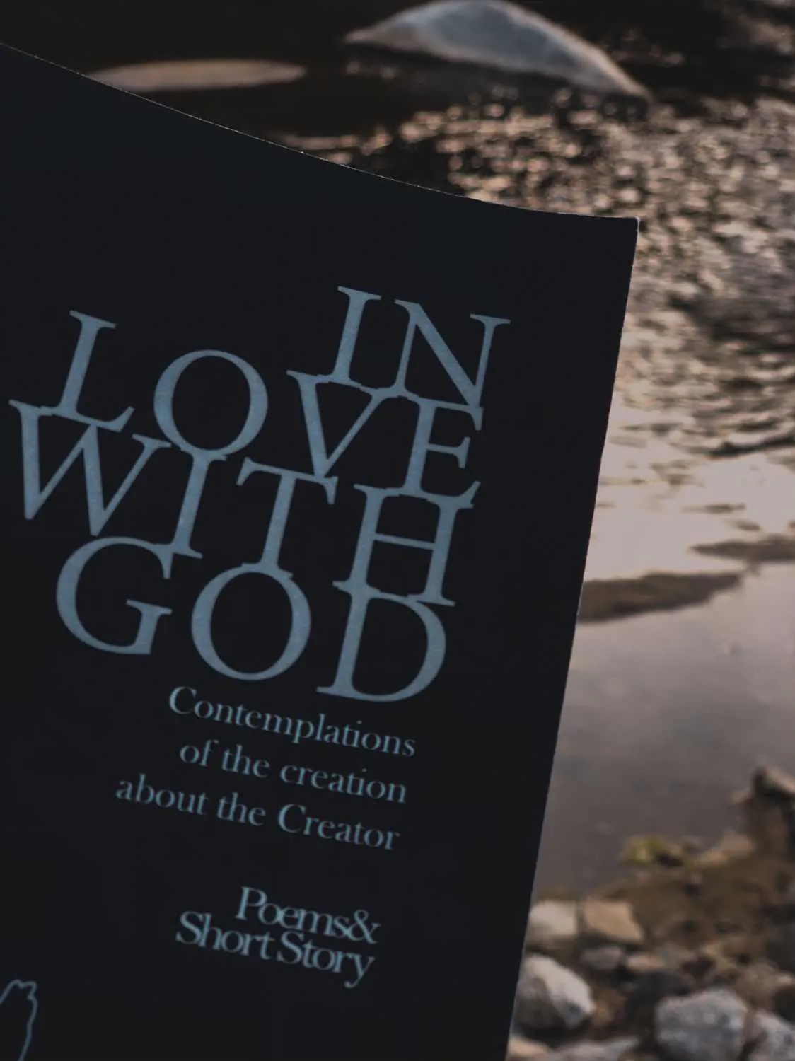 Close-up of the In Love with God cover held over a river at dusk.