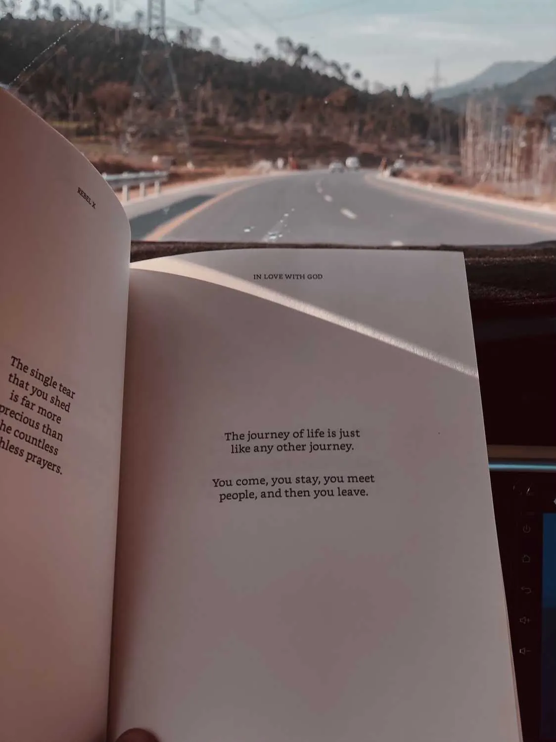 The book lying open on a dashboard, a mountain road unrolling beyond the windscreen.