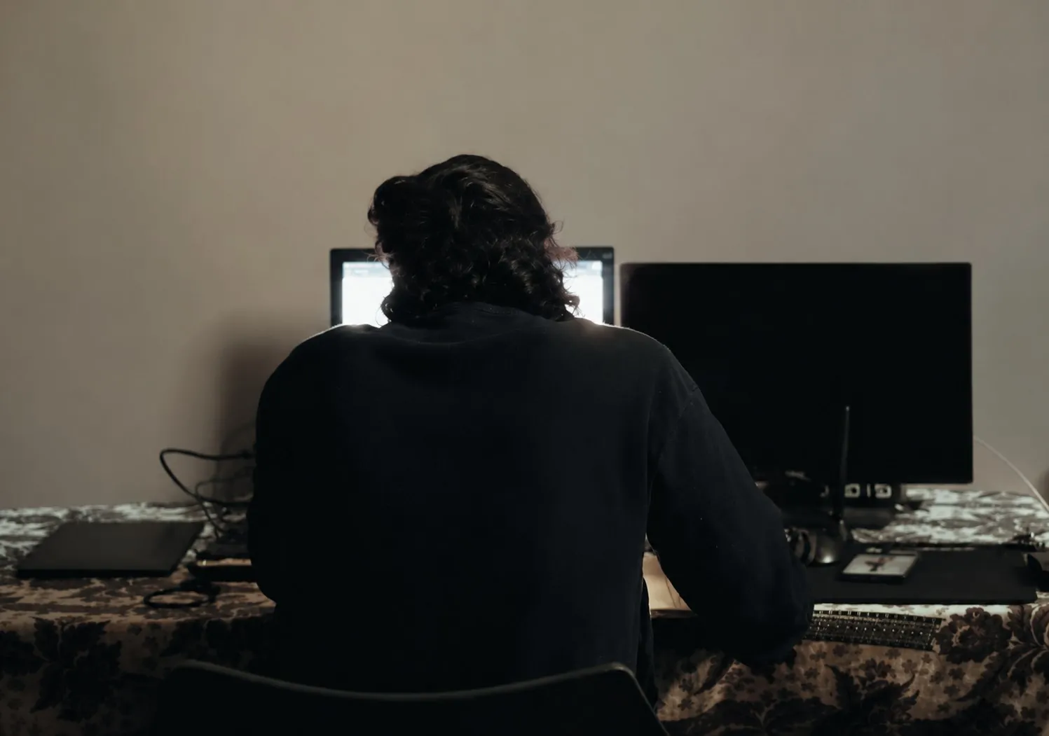 The poet from behind, at a desk with two monitors, working at night.