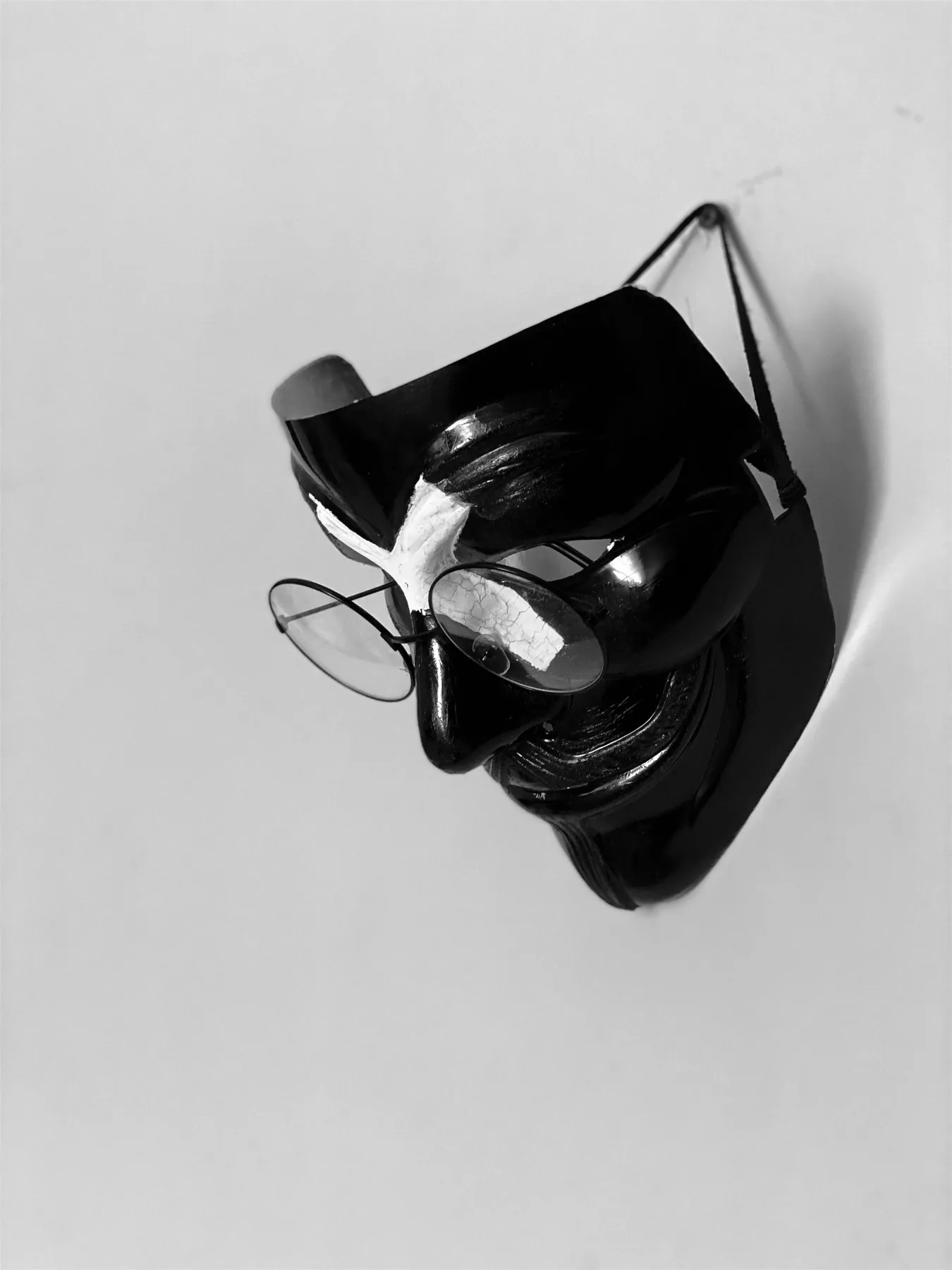 A black mask hanging on a pale wall, the poet's round reading spectacles resting on its nose.