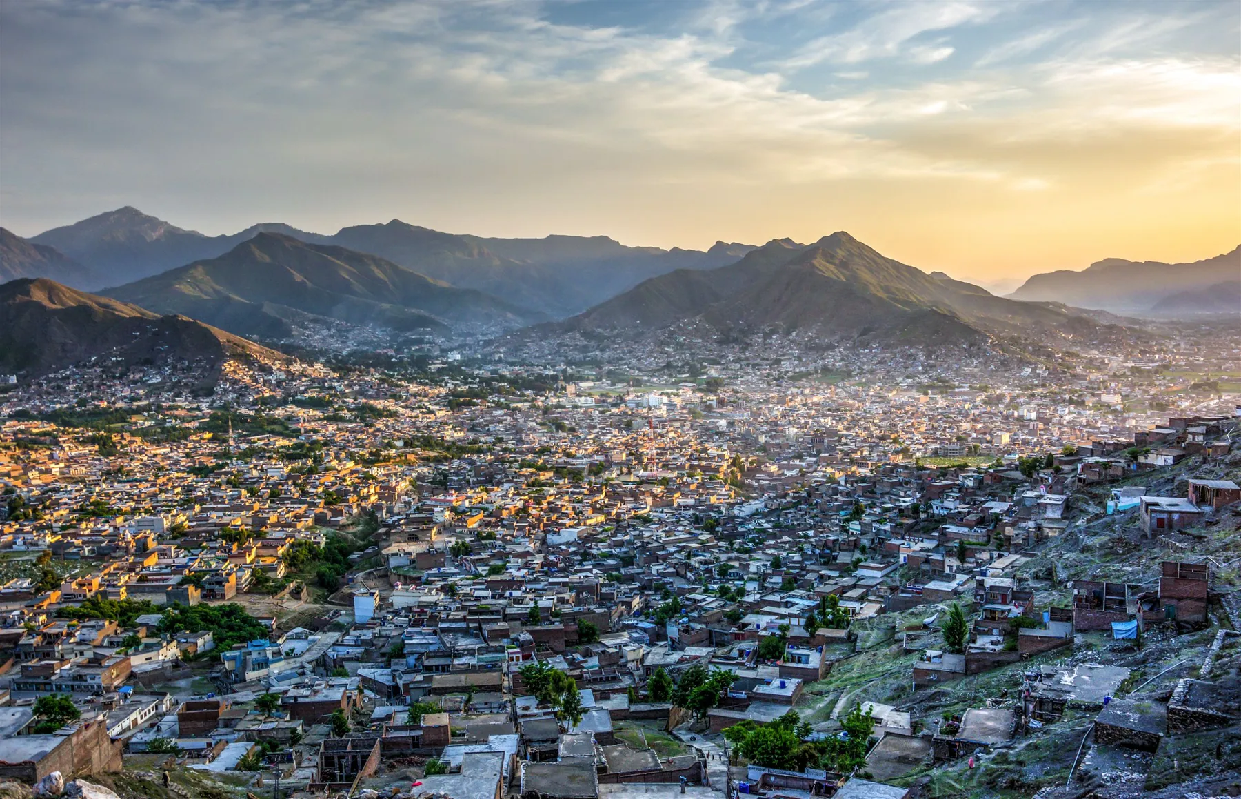 Mingora at golden hour: the city filling the valley floor, ringed by mountains.