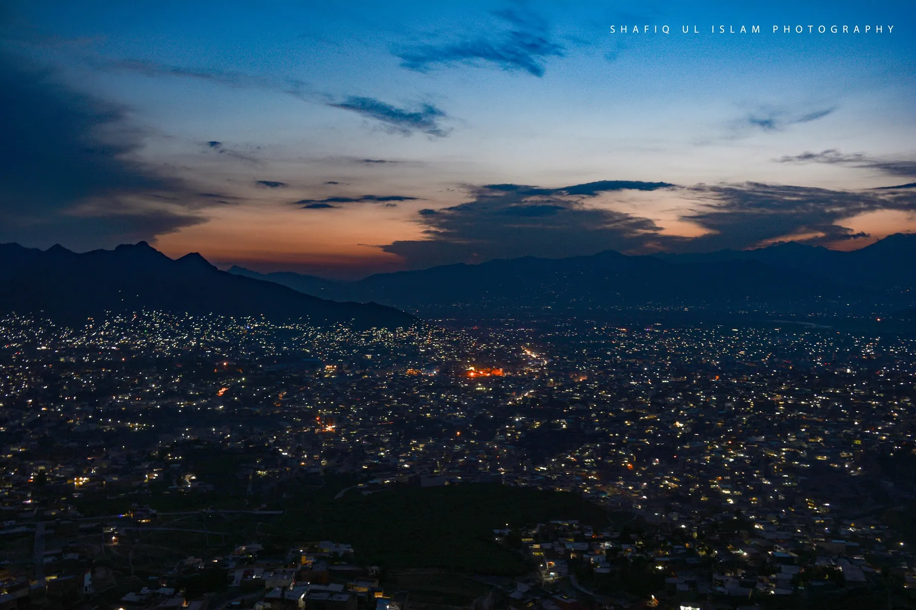 Mingora at night: thousands of lights scattered across the dark valley under the last of the sunset.