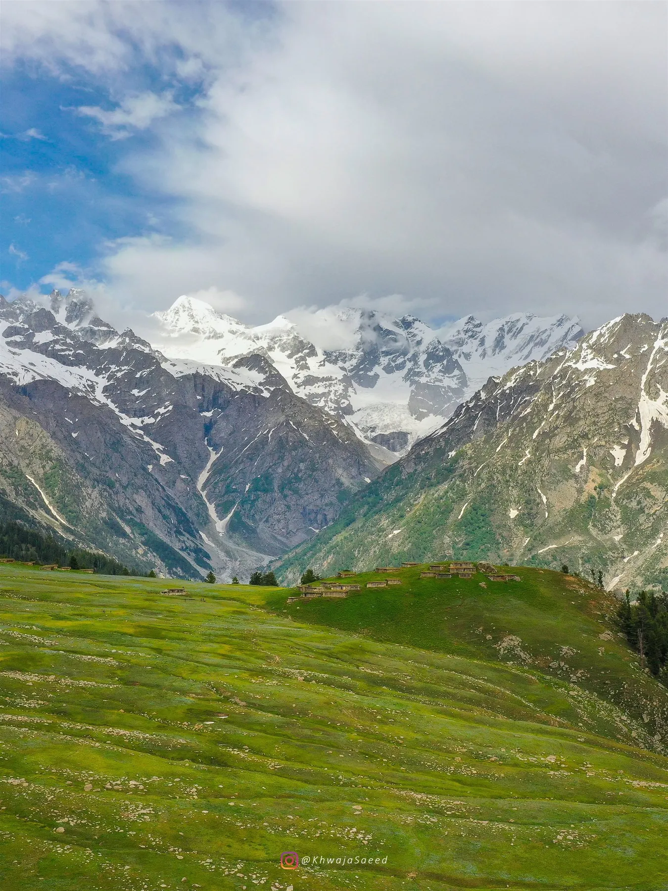 Snow-covered peaks above green highland meadows and stone huts in Swat.